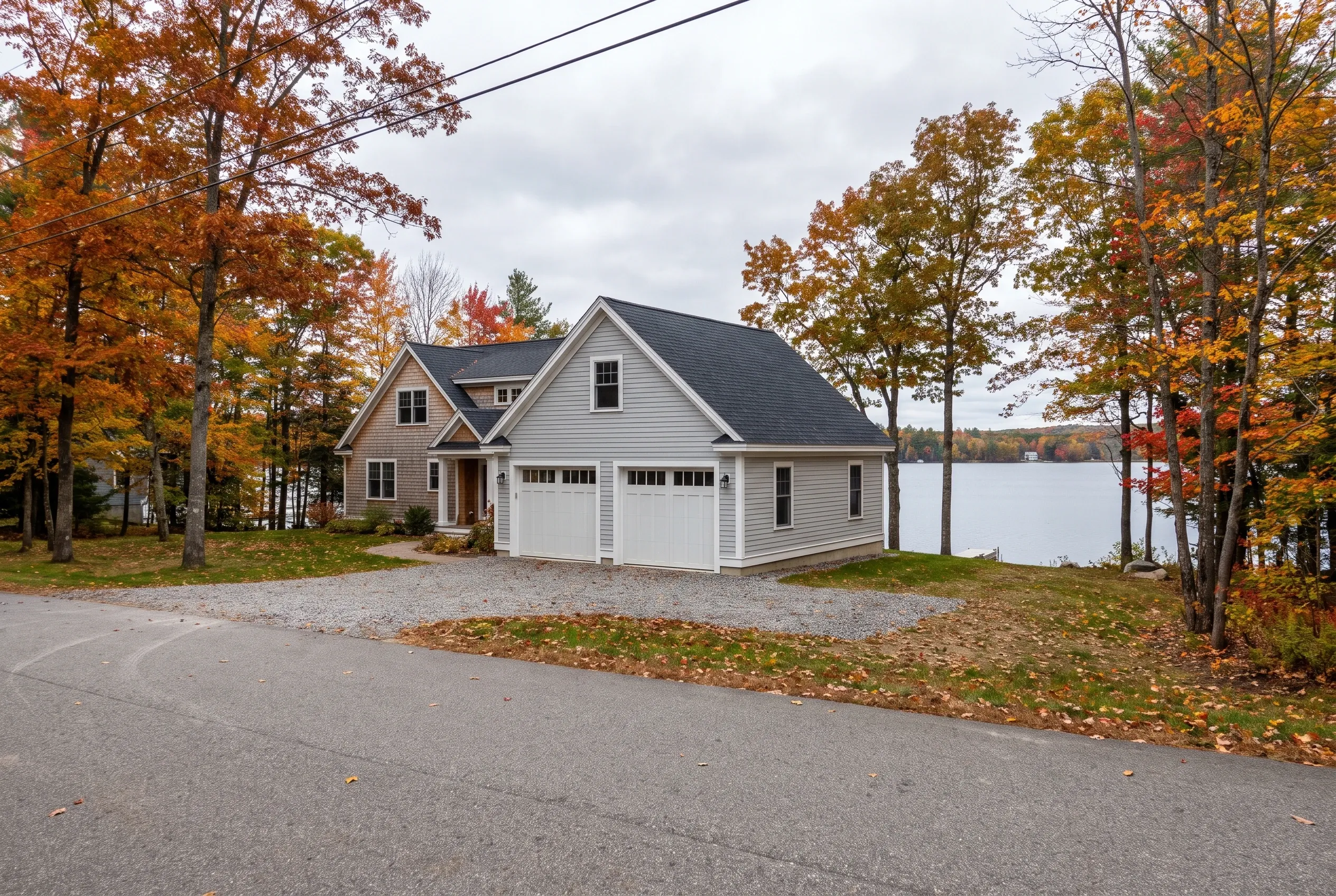 Detached two-bay garage in Manchester, ME: White vinyl-sided garage with dark roof situated on lakefront property surrounded by autumn foliage.