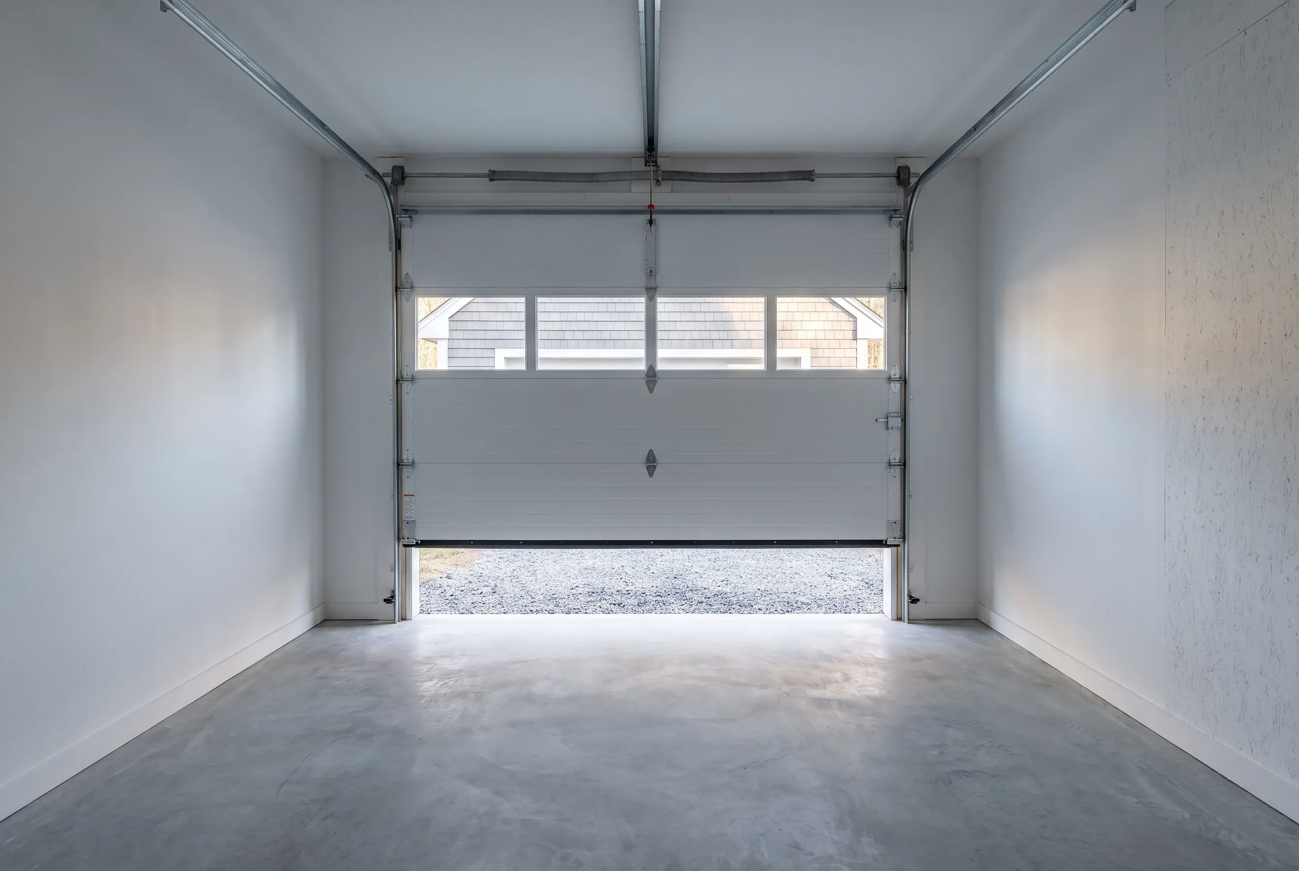 Single-bay garage in Windsor, ME: Interior view of empty garage with white walls, concrete floor, and open garage door showing gravel driveway outside.